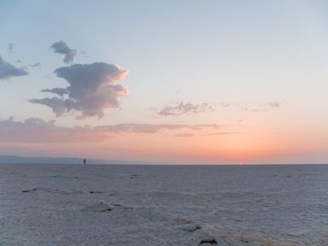 Man meets sunrise alone in Sahara desert. Salt crust on a desert surface. Egypt.