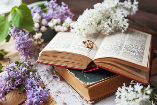 Pair of wedding rings with diamond. Rustic background with old books and lilac flowers. Retro background.