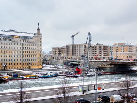 Ships with construction equipment are in Moscow-river under the bridge. Reconstruction of Bolshoy Moskvoretsky Bridge. Winter cloudy day in Moscow, Russia.
