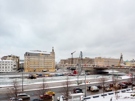 Ships with construction equipment are in Moscow-river under the bridge. Reconstruction of Bolshoy Moskvoretsky Bridge. Winter cloudy day in Moscow, Russia.