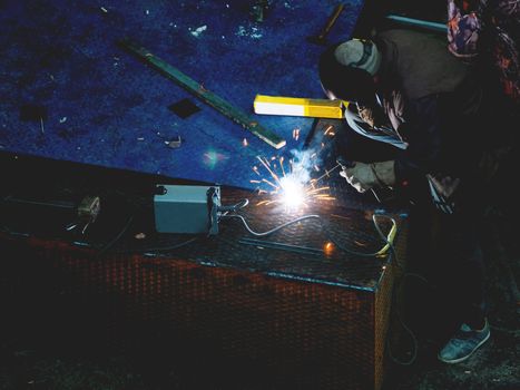 Metal welding. Worker in a welding mask repairs metal steps.