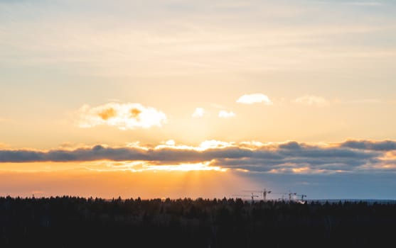 Sunset over forest with silhouettes of construction cranes. Construction of new apartment building. Krasnogorsk, Russia.