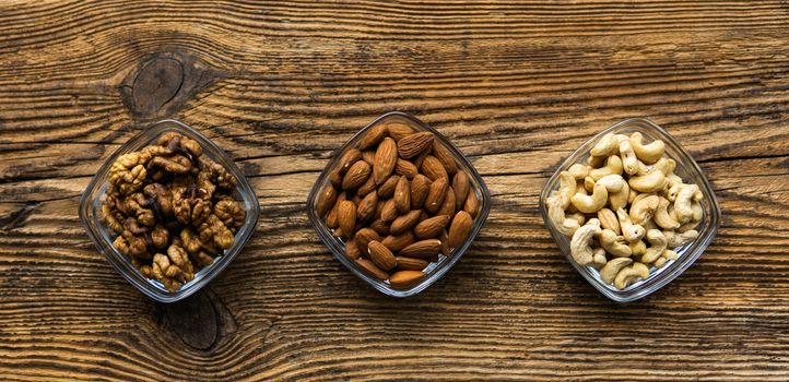 Almond, walnut and cashew in a small plates which standing on a wooden vintage table. Nuts is a healthy vegetarian protein and nutritious food. Nuts on rustic old wood