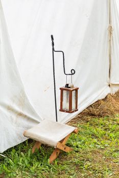 Antique lantern with candle and camp chair at the entrance to the tent. Historical reconstruction of 19th century.