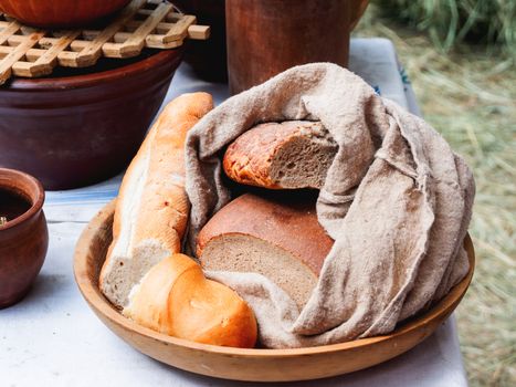 Wooden plate with different kinds of bread. Homespun napkin and tablecloth. Vintage dinnerware and old fashioned household items on historical festival Times and Epochs. Moscow, Russia.