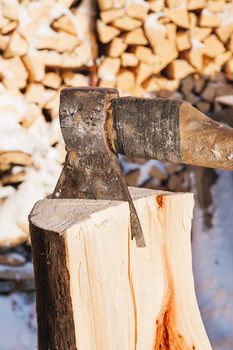 Axe in a wooden deck. Winter sunny day. Rural background with folded pile of firewood.