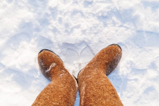 Russian traditional winter footwear - valenki. Winter sunny day, top view on feet felted wool boots.