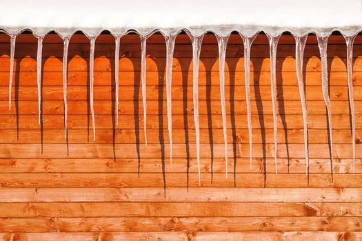 Long icicles on wooden wall in sunny winter day.