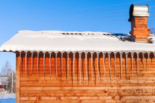 Long icicles on wooden wall in sunny winter day.