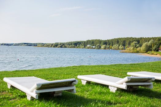 White wooden chaise lounges on the bank of the Ilyinsky reservoir. Outdoor recreation. Moscow region, Russia.