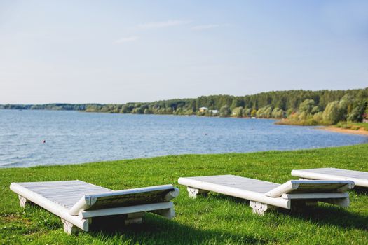 White wooden chaise lounges on the bank of the Ilyinsky reservoir. Outdoor recreation. Moscow region, Russia.