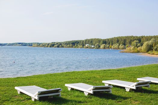 White wooden chaise lounges on the bank of the Ilyinsky reservoir. Outdoor recreation. Moscow region, Russia.
