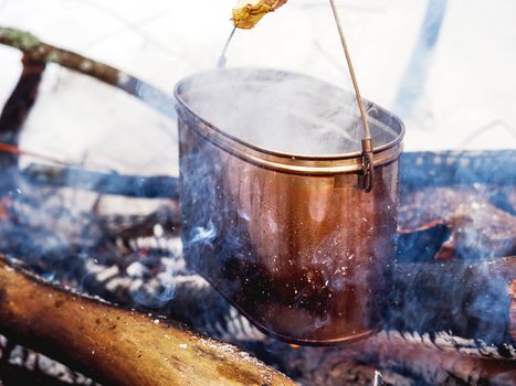 Cooking soup on a fire pot. Winter camping in forest.