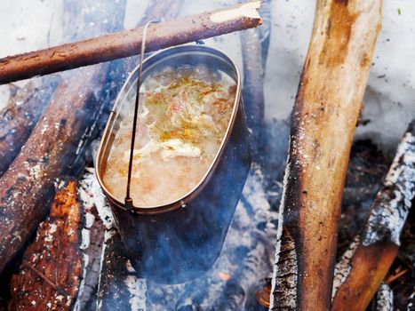 Cooking soup on a fire pot. Winter camping in forest.