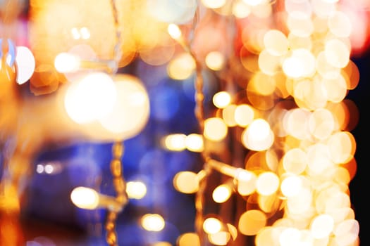 Defocused night street lights, blurred colorful bokeh background. Holiday colorful lanterns and light bulbs garlands.