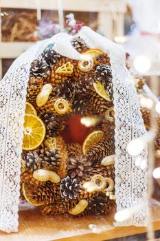 Christmas wreath made with pine and fir cones, dried oranges, peanuts and baked bagels. Hand made New Year decoration with lace bow.