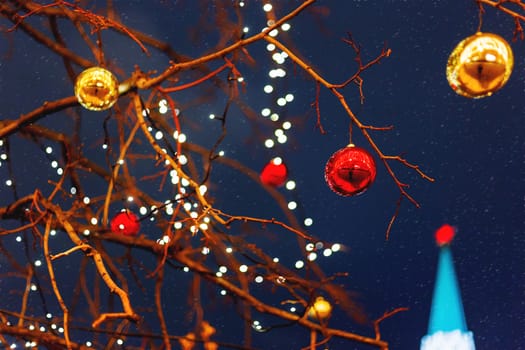 Streets of Moscow decorated for New Year and Christmas celebration. Tree with bright red and yellow balls. The St.Nicholas (Nikolskaya) tower of Kremlin on the background. Russia.