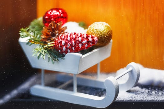 Christmas and New Year decorations - white wooden sledge with bright sparkling balls and fir tree branches.