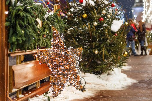 Christmas and New Year background with fir trees and bright decorative star - outdoor decoration made of willow branches with light bulbs garland.