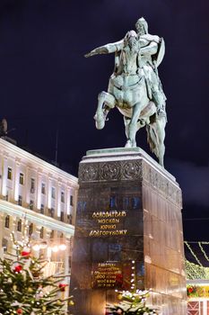 Monument to prince Yury Dolgorukiy, the founder of Moscow, on Tverskaya square (text on pedestal). Street decorated with light bulbs for New Year and Christmas celebration. Russia.