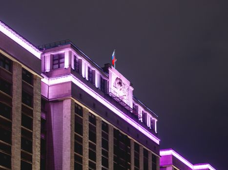 Building of State Duma of Russia. Illuminated top of building with national flag.