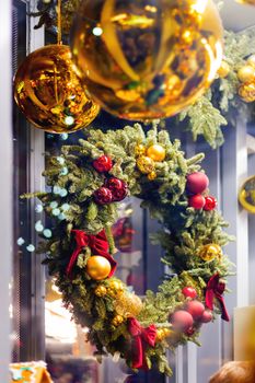 Christmas wreath made of fir tree branches with red and golden ribbons, balls and bows. Shining New Year decorations.