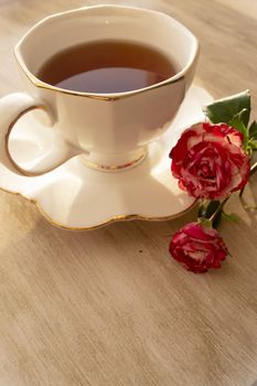 Cup of tea in a china cup and saucer, on a distressed table and roses