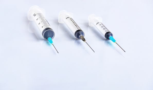 Three syringes of different capacity on a white table, prepared for injection in the hospital with copyspace for text.