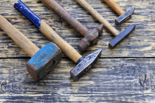 Old worn iron hammers with wooden handles lie on a wooden table.