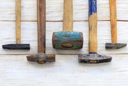 Old worn iron hammers with wooden handles lie on a white wooden table.