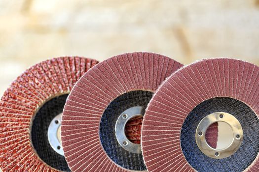 A part of flap grinding wheels of different grain for sanding wood and rusty metal on a light beige background in unsharpness, close-up.