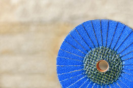 A part of a petal grinding wheel of blue color for sanding wood and rusty metal on a light beige background in unsharpness, close-up.