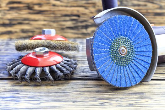 Angle grinder with grinding disc brushes and abrasive wire brushes lies on the background of a wooden table.