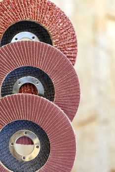 Flap grinding wheels of different grain for sanding wood and rusty metal one on top of another vertical on a light beige background in unsharpness, close-up.