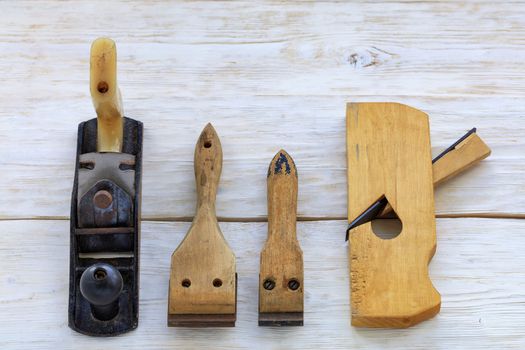 Old carpentry hand tools, planers and cycles lie on a white wooden table.