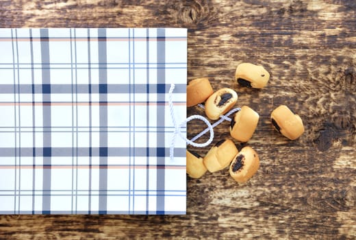 Small poppy buns spilled onto an old textured wooden surface from a tartan-painted paper bag.