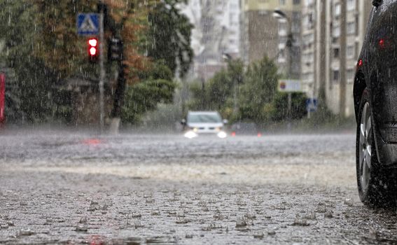 Torrential rain at crossroads and red light reflected in the flow of water on a city street.