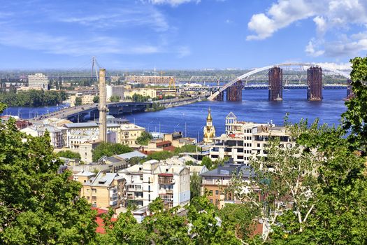 The Dnipro River with various bridges on a bright summer day and a view of the old Podol district of the city of Kyiv.