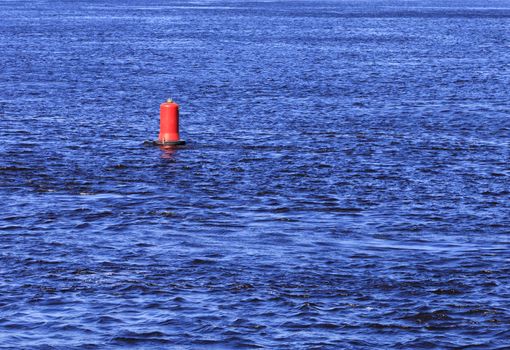 View of the blue waters of the river and the red buoy, which sways on the waves.