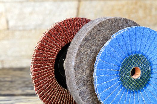 Grinding discs of various grains for grinding wood and rusty metal together with felt circle on a light beige background in unsharpness, close-up.