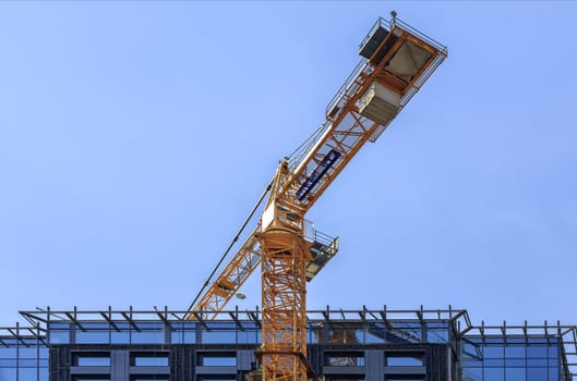 A fragment of the roof of the facade of a house under construction, a modern building is being built, a tower crane is located above the roof against a blue sky.