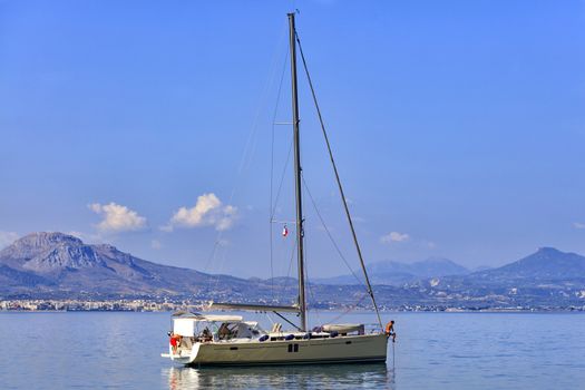 Sailing sea yacht anchored in the morning haze in the Corinthian bay against the backdrop of a mountain range and blue with small clouds of sky.