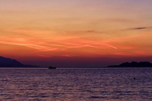 The silhouette of a sea boat that goes along the water surface of the sea against the backdrop of a beautiful, vibrant sunset on the Gulf of Corinth. Loutraki, Greece.