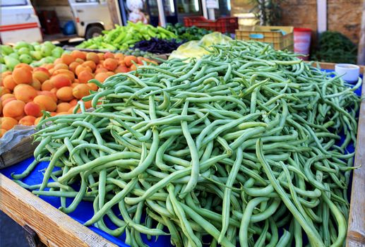 Bright background of fresh vegetables and fruits, green beans, apricots, pears, plums lying in trays in the market and attracting attention.