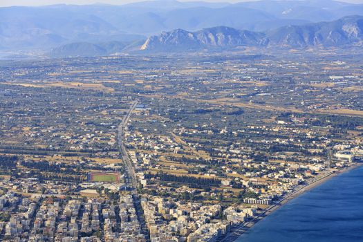 View of the central street of Loutraki leading to the Corinth Canal and the sea promenade of Loutraki, the sea of the blue Corinthian Gulf in Greece from a bird's eye view against the backdrop of massive mountains.
