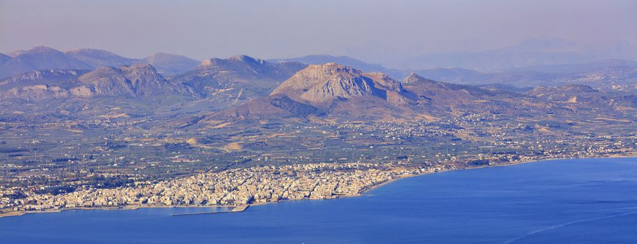View of the city of Corinth on the coast of the Ionian Sea, the sea promenade, the sea of the blue Corinthian Gulf in Greece from a bird's eye view on the background of massive mountainsof the Acropolis and of Sisyphus Mountain.