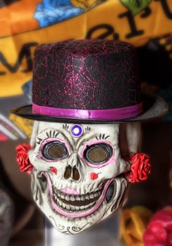 Halloween, skull doll with a smile, decorated with female makeup in a black and red hat, isolated on a worn background.