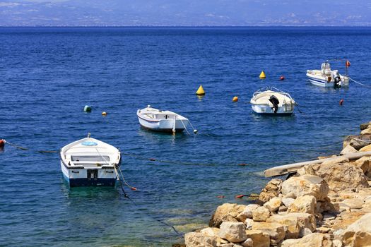 Powerboats and boats moored off the rocky shore of the Ionian Sea against the backdrop of the blue of Corinth Bay