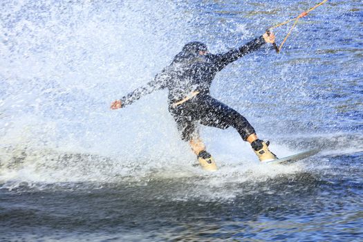 A wakeboarder rushes through the water at high speed creating a cloud of spray around himself.