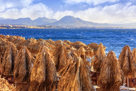 The tops of beach umbrellas are collected, the embankment of the sea is illuminated by the rays of the setting sun against the horizon with mountain ranges in haze and blur.